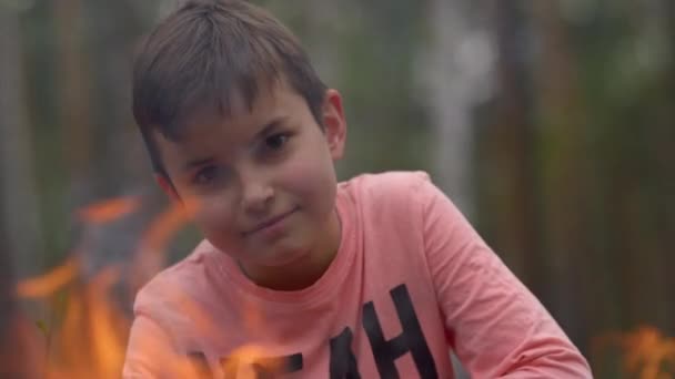 Adolescent jongen op zoek met antipathie door lijn van vuur vlam in het bos. — Stockvideo