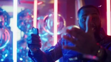 Neon arka planda gülümseyen afro adam konuşuyor. Kulüpte cep telefonu tutan adam.