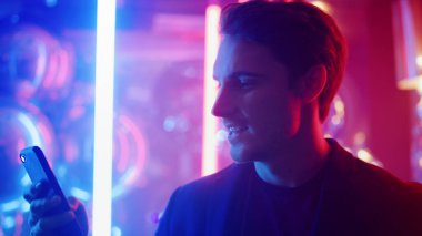 Gece kulübünde akıllı telefon kullanan yakışıklı bir adam. Partide dans eden gülen adam.