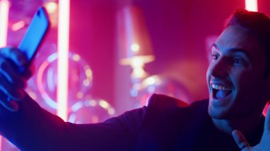 Sevimli erkek, neon arka planda selfie çekiyor. Gece kulübünde fotoğraf çeken adam.