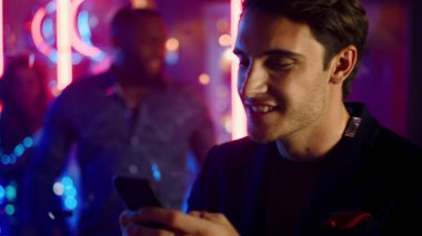 Gece kulübünde mesaj yazan yakışıklı adam. Telefonu neon arka planda tutan adam.