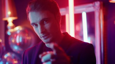 Partide seksi bir adam bardak kaldırıyor. Neon arka planda objektife bakan seksi adam.