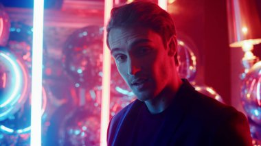 Sevecen adam arka planda neon ışıklarda gülümsüyor. Partide göz kırpan adam