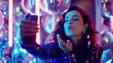 Esmer kadın, neon arka planda akıllı telefon kullanıyor. Partide selfie çeken kız.