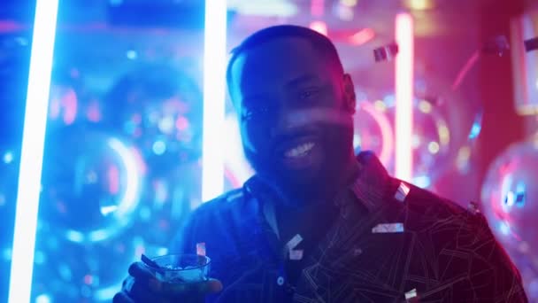 O afro bebe álcool no clube. Homem levantando vidro no fundo de néon. — Vídeo de Stock