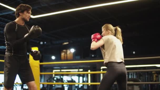 Улыбающийся тренер тренируется с спортсменкой на боксерском ринге. Парный бокс в тренажерном зале — стоковое видео