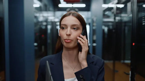 Positiv kvinna som pratar i telefon på kontoret. Damen ser sig omkring i korridoren — Stockfoto