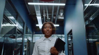 Koridorda el sallayan gülümseyen afro kadın. Dost canlısı iş kadını selam söylüyor.