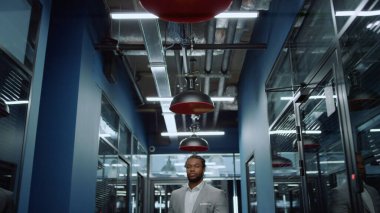 Koridorda objektife bakan Afrikalı Amerikalı bir adam. İş adamı buluşmayı bekliyor.