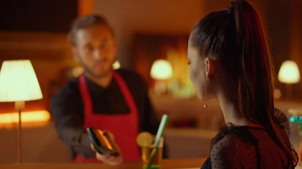 Smiling girl making contactless payment in club. Woman buying cocktail in bar