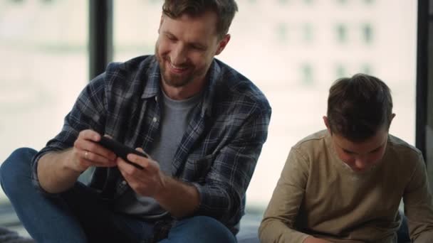 Padre e hijo usando teléfonos inteligentes en casa. Papá y el niño jugando juego móvil en el interior — Vídeos de Stock