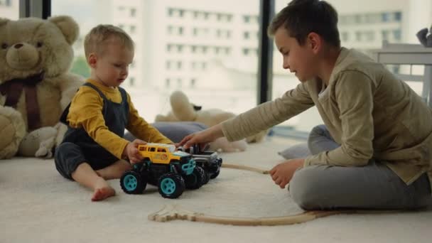 Niños agradables compartiendo coches de juguete en la alfombra. Increíbles niños jugando juntos en interiores. — Vídeos de Stock