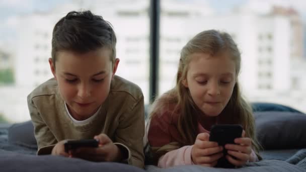 Broer en zus die gokken op mobiele telefoons. Broers en zussen die thuis smartphones gebruiken. — Stockvideo