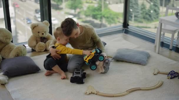 Dva sourozenci se objímají v dětském pokoji. Milí bratři sedící doma na podlaze. — Stock video