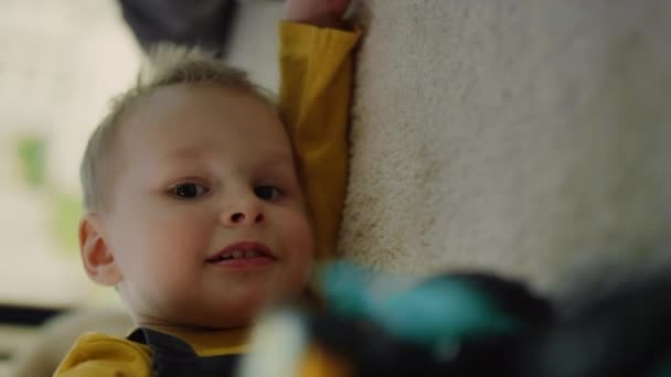 Retrato de niño lindo acostado en la alfombra interior. Divertido niño jugando coche de juguete en el interior. — Vídeo de stock