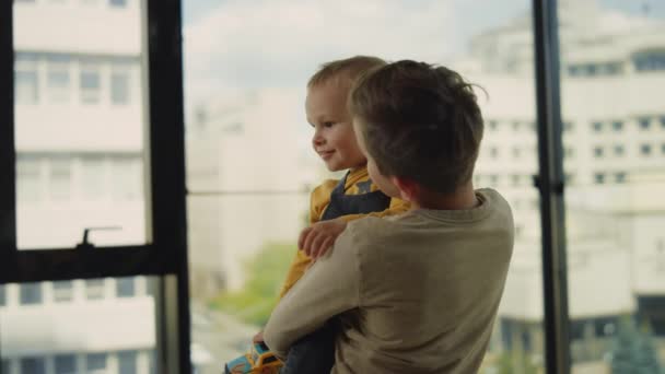 Elder brother holding little kid indoors. Older boy looking after younger. — Stock Video