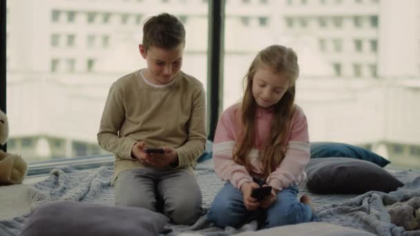 Des enfants assis sur le sol avec des téléphones portables. Frères et sœurs jouant à des jeux mobiles. — Video