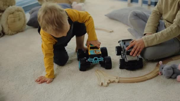 Funny boy playing with toy truck on floor. Siblings spending time home interior — Stock Video