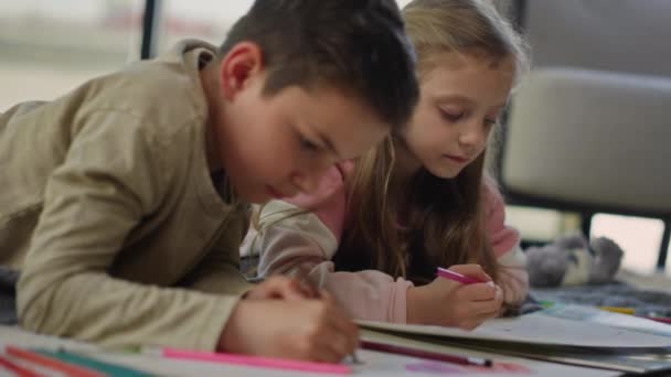 Jongen meisje kleuren foto 's op de vloer. Schattige broers en zussen schilderen in schetsboeken huis — Stockvideo