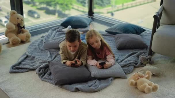 Frères et sœurs utilisant des smartphones maison. Beaux enfants jeux téléphones mobiles. — Video