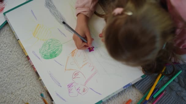 Невідома дівчина лежить на підлозі з кольоровими олівцями. Креативна дитина малює картинку будинку — стокове відео