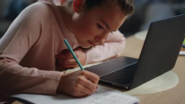 Школьница делает домашнее задание рядом с ноутбуком в помещении. Девочка-подросток учится дома. — стоковое видео
