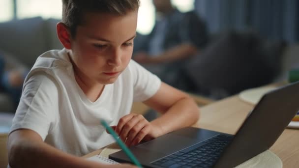 Ребенок пишет домашнее задание дома. Серьезный мальчик, использующий ноутбук для дистанционного обучения. — стоковое видео