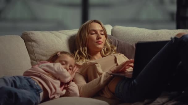 Mamá usa el portátil junto a su hija en el sofá. Chica durmiendo mamá hombro — Vídeos de Stock