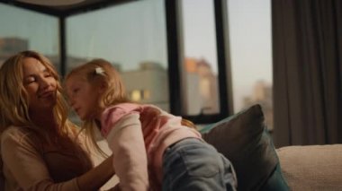 Anne, evdeki kanepede kızına sarılıyor. Anne ve çocuk birlikte vakit geçiriyorlar..