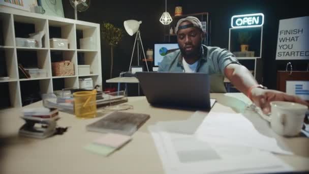 Fokuserad afrikansk amerikansk affärsman dricker kaffe i sen coworking. — Stockvideo