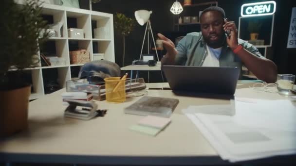 Frustrado africano masculino profesional hablando en el teléfono móvil en la oficina oscura. — Vídeos de Stock