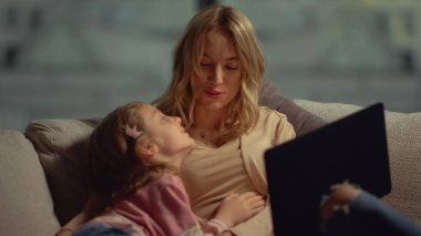Mutlu anne ve kız birlikte vakit geçiriyorlar. Anne koltukta çocuğa sarılıyor..
