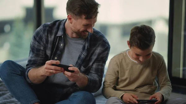 Apa és fia mobiltelefonokat játszanak. Apa és fiú kémkednek egymás után okostelefonok. — Stock Fotó