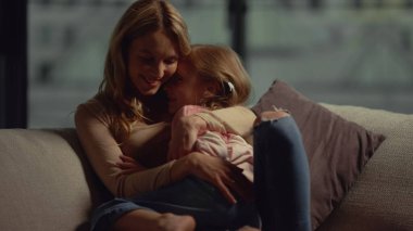 Anne kızını kanepede kucaklıyor. Anne ve çocuk evde birlikte vakit geçiriyorlar..