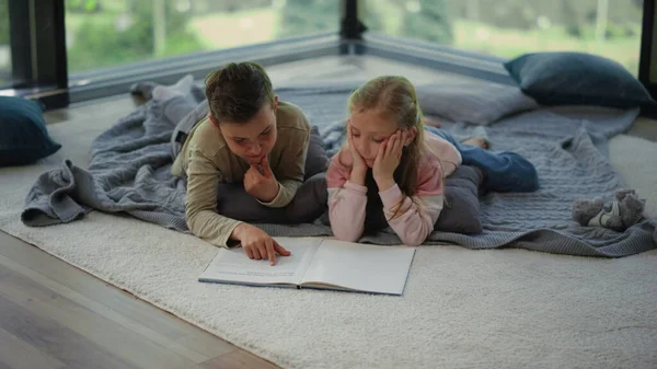 Мальчишка лежит на ковре с книгой. Братья и сёстры ищут информацию в учебнике — стоковое фото