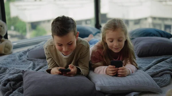 Tricky kids addicting mobile games. Siblings playing on smartphones at home.