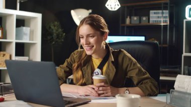 Karanlık ofiste gülümseyen kız konuşuyor. İşte kahve içen meşgul bir kadın..