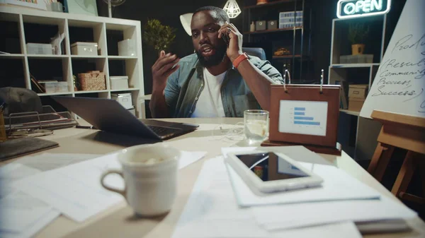 Emotionaler afrikanischer Geschäftsmann beim nächtlichen Coworking mit dem Handy. — Stockfoto