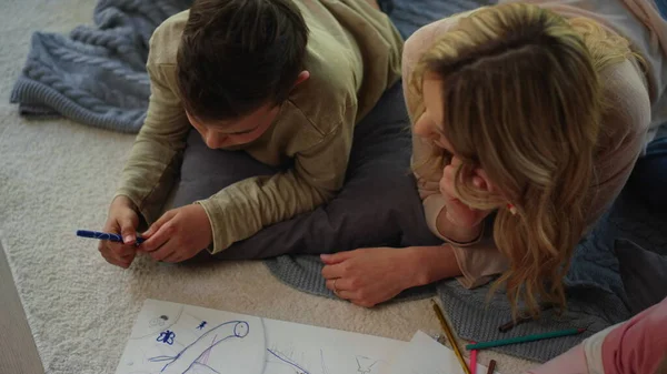 Anya kreatív testvéreket figyel. Anya tanácsolja a gyerekeknek, hogyan rajzoljanak képet. — Stock Fotó