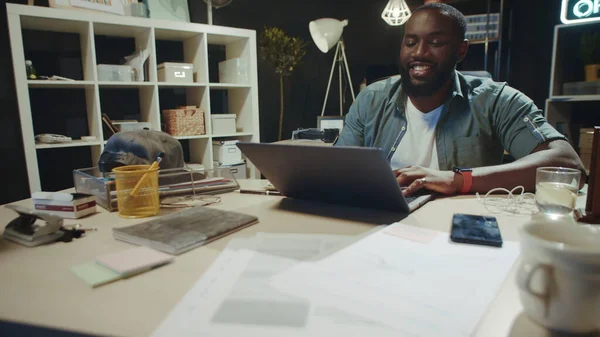 Fröhlicher afrikanisch-amerikanischer Geschäftsmann kommuniziert auf Laptop im Hipster-Büro. — Stockfoto