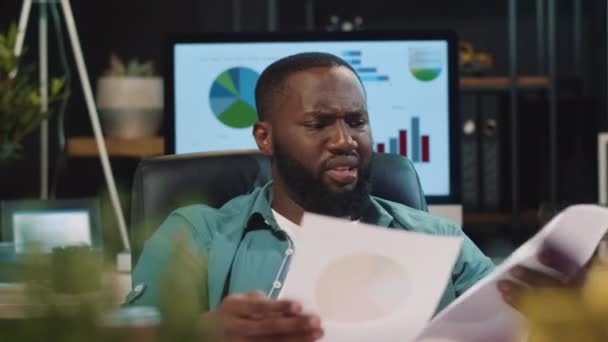 Κοντινό πλάνο απογοητευμένος αφρικανός hipster τύπος κοιτάζοντας διαγράμματα στο νυχτερινό γραφείο — Αρχείο Βίντεο