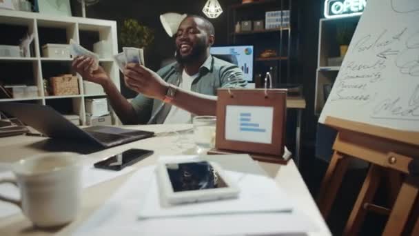 Vrolijke Afro-Amerikaanse zakenman met dollars rekeningen laat op de avond kantoor. — Stockvideo