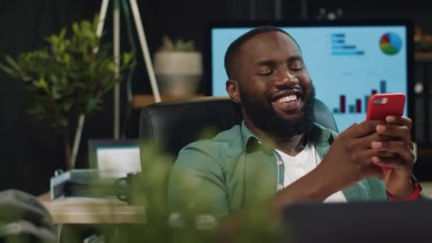 Closeup χαρούμενη afro επιχειρηματίας δακτυλογράφηση μήνυμα στο smartphone σε hipster γραφείο — Αρχείο Βίντεο