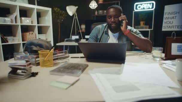 Hombre africano exitoso disfrutando de la conversación del teléfono móvil en el espacio de trabajo. — Vídeos de Stock