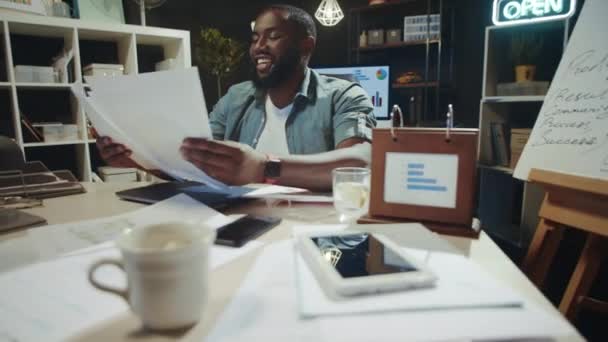 Retrato del hombre de negocios afro sonriente satisfaciendo con documentos en el lugar de trabajo. — Vídeos de Stock