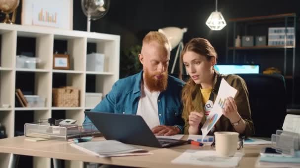 Jovem casal de negócios mostrando documentos na frente da tela do laptop no escritório — Vídeo de Stock