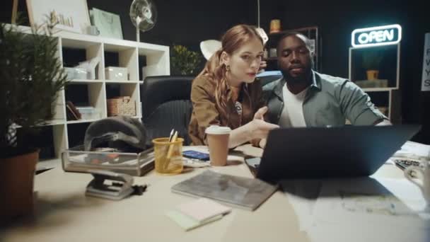 Африканский американец обнимает удивленную женщину возле ноутбука в темном офисе. — стоковое видео