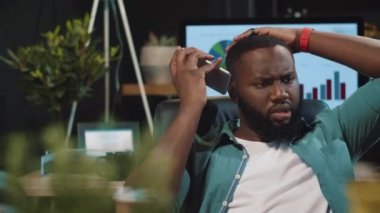 Odaklanmış Afro-Amerikan hipster adam gece ofisinde cep telefonundan konuşuyor..
