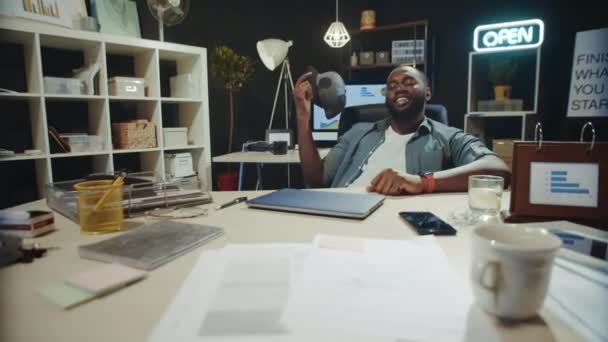 Cheerful african american businessman fanning face with cap in late coworking. — Stock Video