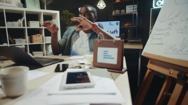 Portrait of playful african american guy having fun near laptop in dark office. — Stock Video